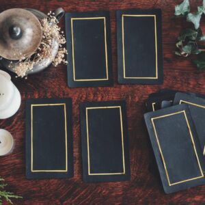 Tarot 4 card spread laid on a nature display (flat lay) . Hand made tarot cards on a dark wooden table surrounded with evergreens, ivy and white candles. Black cards with golden shiny rectangular rim